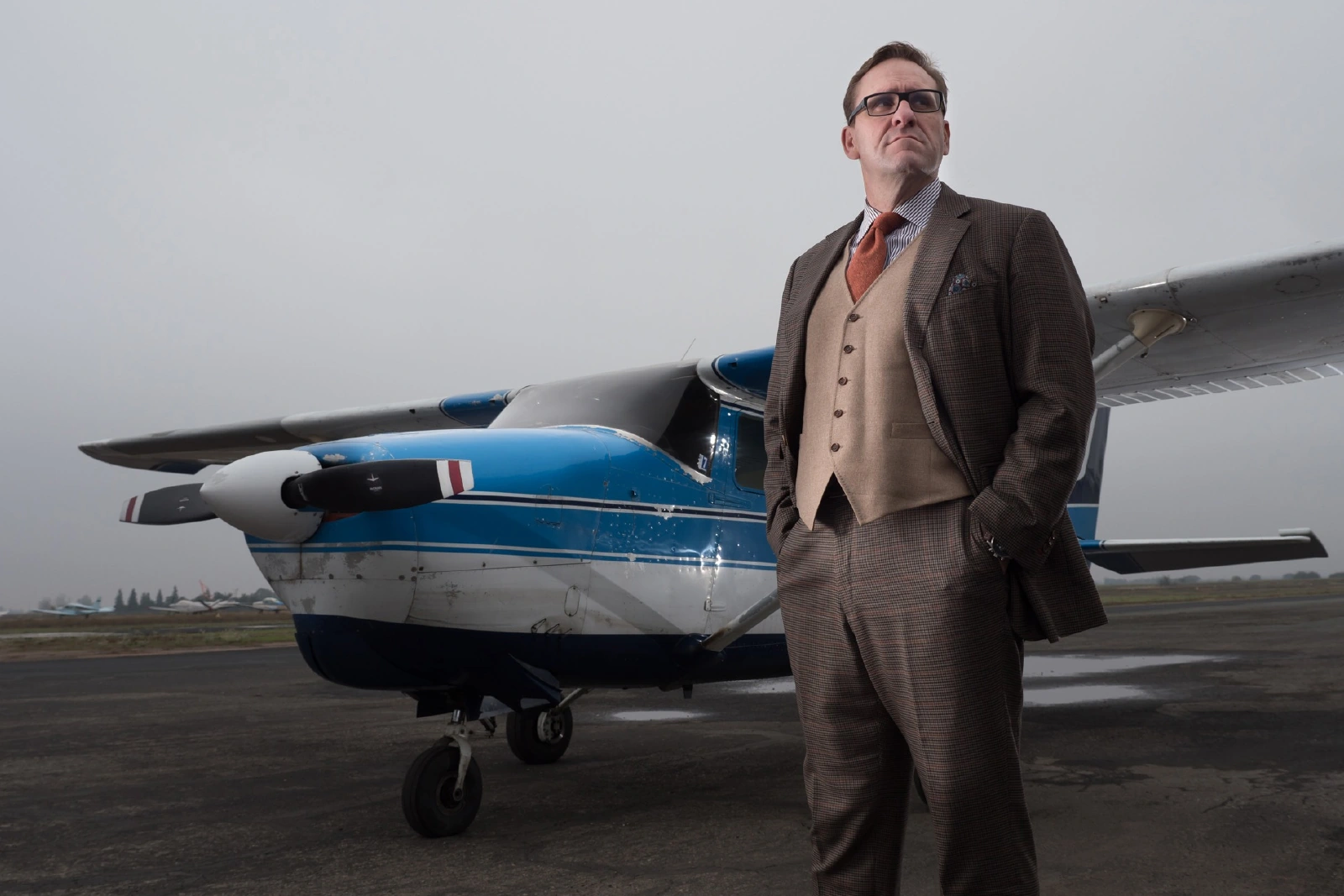 Original flash-lit portrait of a man beside a blue aircraft under an overcast sky
